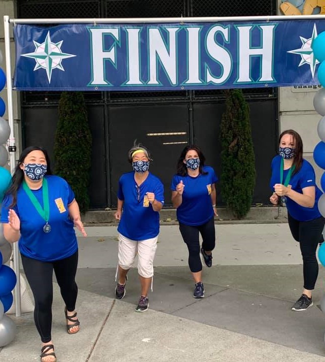 Four women standing at the 2020 Refuse To Abuse 5K Finish Line. They are all wearing masks and starting to run towards the camera.