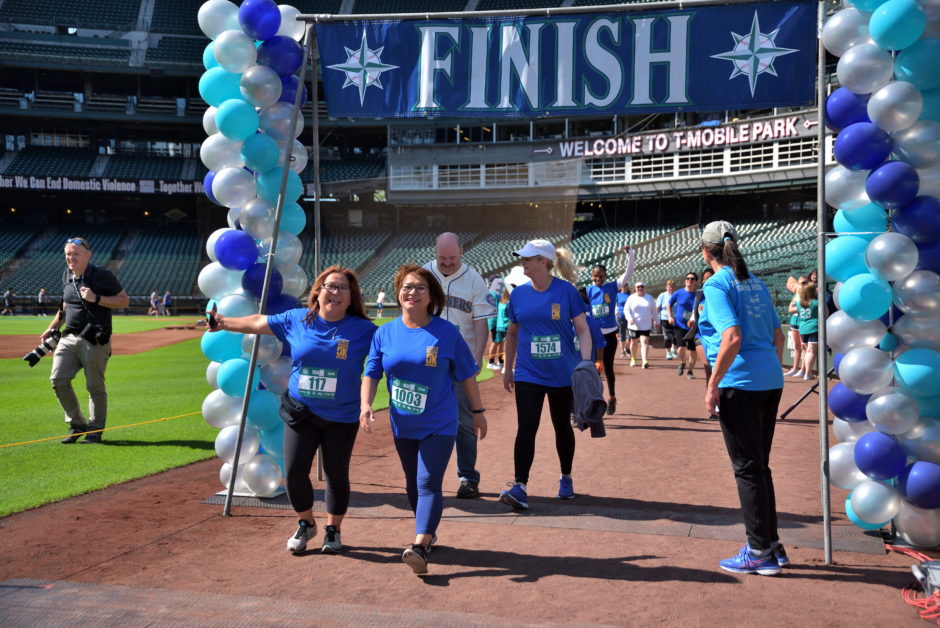 Photo of finish line at Refuse To Abuse 5K at T-Mobile Park. Group of people are finishing the event and smiling.