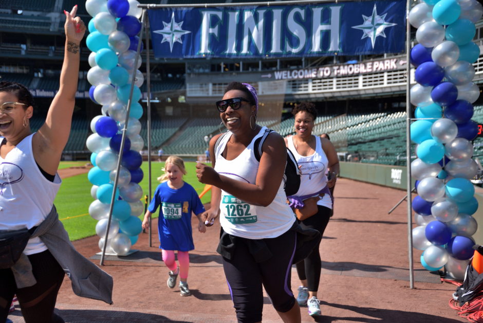 Photo of finish line of Refuse To Abuse 5K at T-Mobile Park. Group of people are finishing the event and smiling.