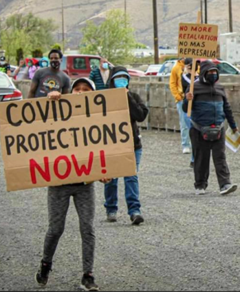 Protesters marching with sign "Covid-19 protections now!"
