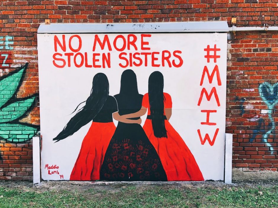 A mural by Maddie Sanders that says "no more stolen sisters. #mmiw." There is an image of three Indigenous women with red and black skirts facing away.
