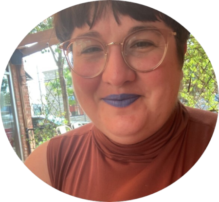 Picture of Heather, a person with short dark brown hair, light framed glasses, and blue lipstick, smiling at the camera.