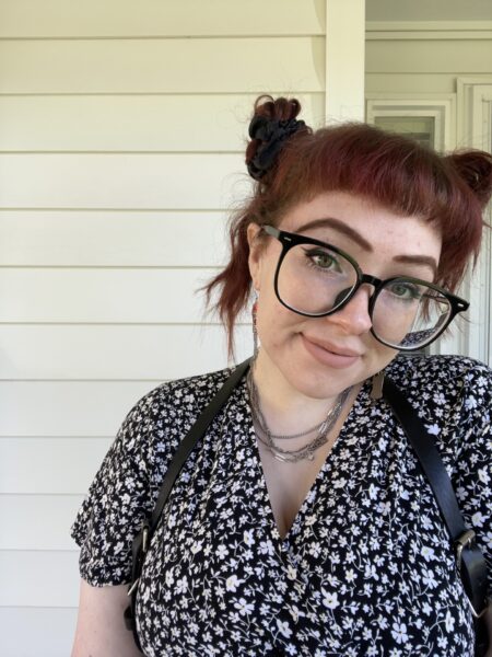 Image of Jessie, smiling with brownish-red hair and black framed glasses.